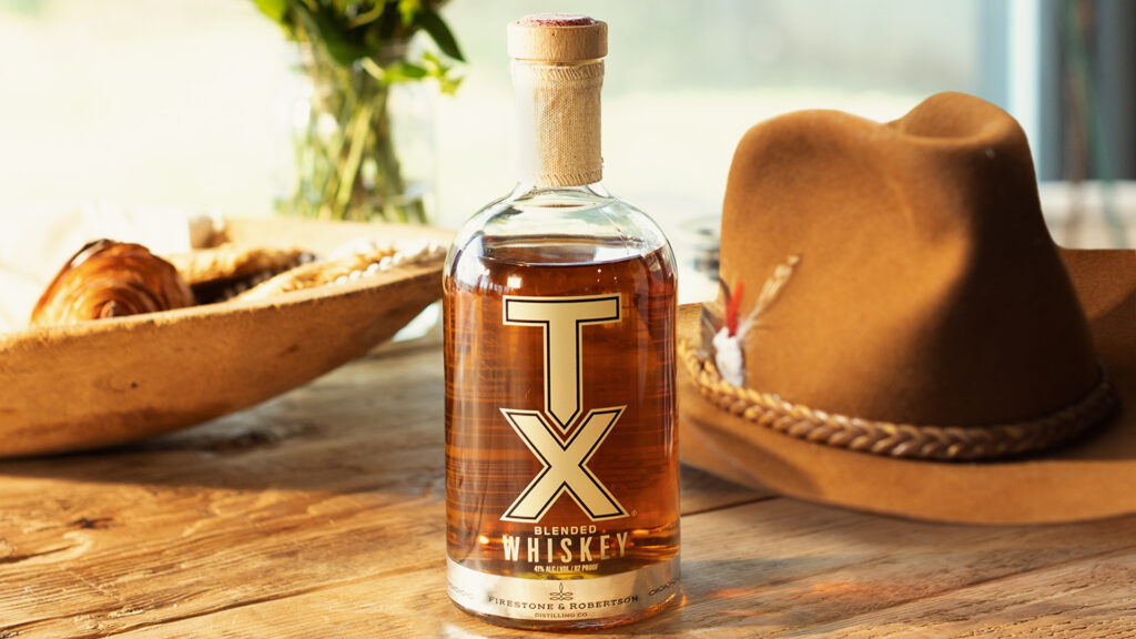 A bottle of TX Blended Whiskey in front of a cowboy hat.