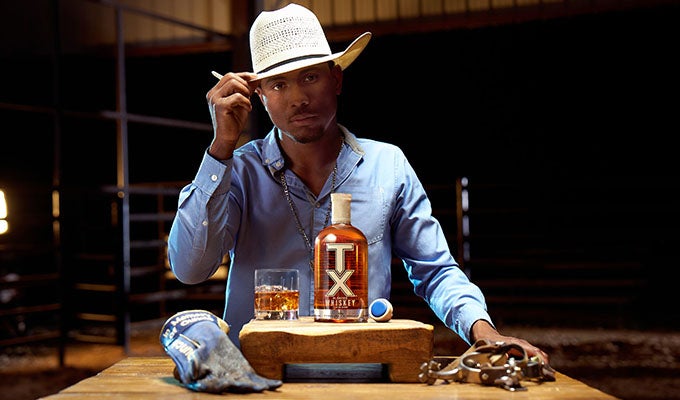 A bottle of TX Whiskey sits in front of Ezekiel Mitchell who is tipping his white cowboy hat